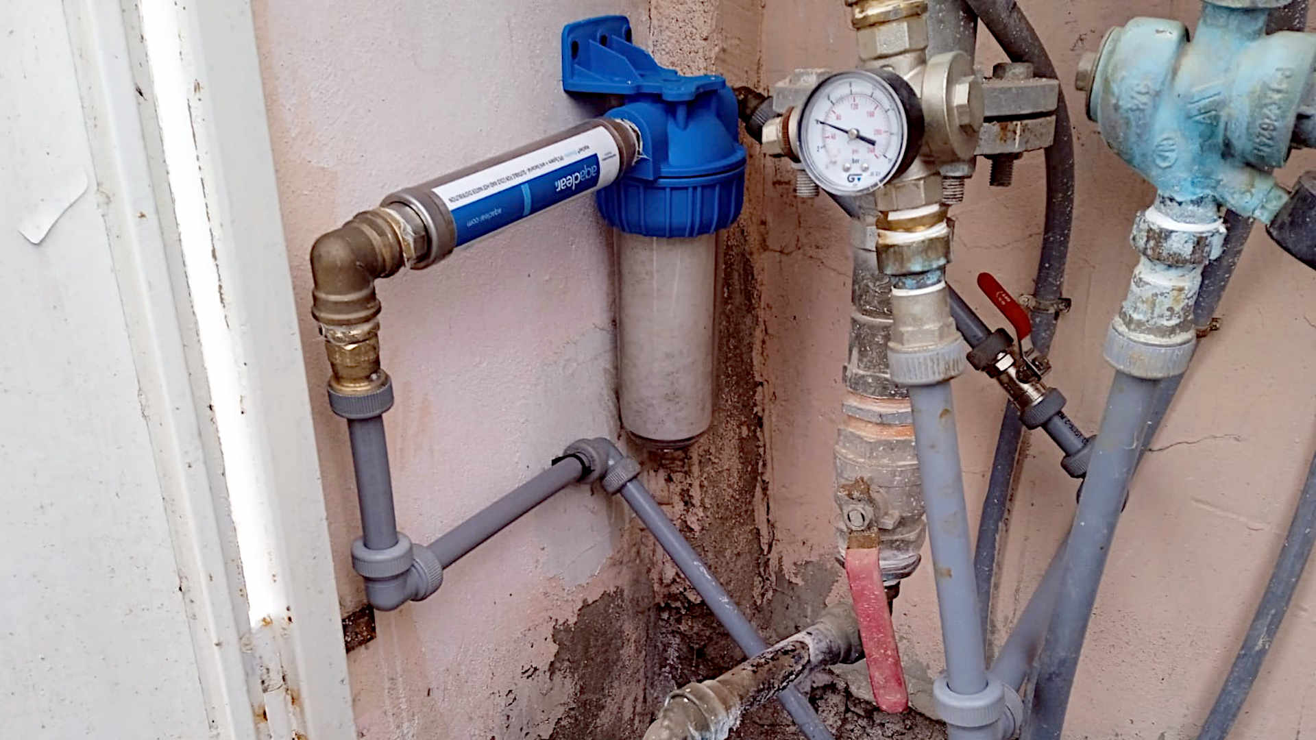 Dispositivo Aqaclear AC820 Hogar instalado en la entrada de agua de un recinto. Se ve el contador de agua y un prefiltro para sedimentos.